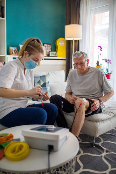 Physiotherapist applying electro stimulation in physical therapy to a senior man knee after injury.