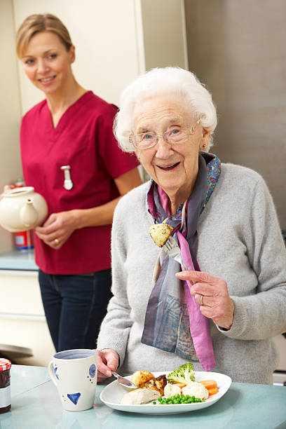 Senior woman with carer eating meal at home smiling at camera